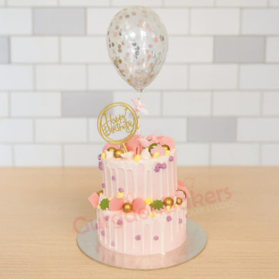 A beautifully decorated birthday cake with pink frosting, golden spheres, and a balloon