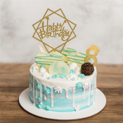 A beautifully decorated birthday cake with blue drip icing and a joyful golden 'Happy Birthday' topper