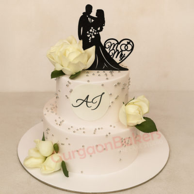 Elegant two-tier anniversary cake with white roses and a cake topper featuring a couple