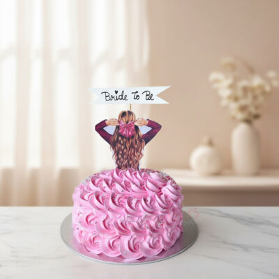 A beautifully designed pink Bride To Be cake with a girl figurine and floral accents