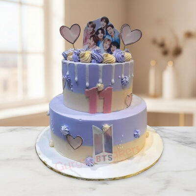 Two-tier BTS themed cake with drips and decorative heart toppers.