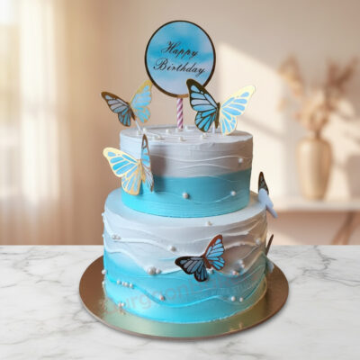 Two-tiered butterfly cake with blue and white frosting, decorated with butterfly toppers and ready for a birthday celebration.