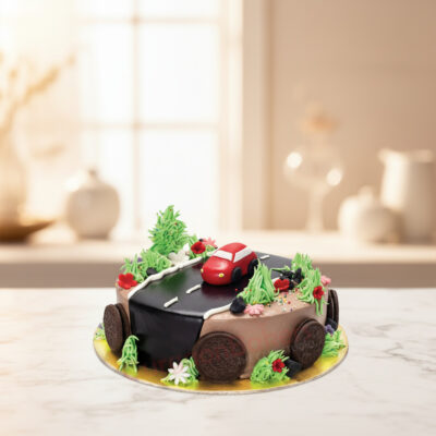 A colorful car cake for a toddler's birthday featuring a red car on a road with flowers and greenery.