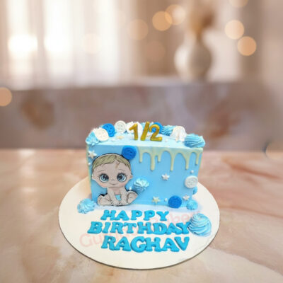 Half birthday cake decorated in blue with a baby character and text 'HAPPY BIRTHDAY RAGHAV'