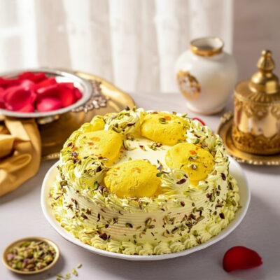 A beautifully decorated Rasmalai Cake topped with yellow rasmalai pieces and pistachio garnishing.