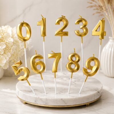Gold metallic number candles 0 to 9 on white sticks displayed on a marble stand for birthday cake decoration in Gurgaon