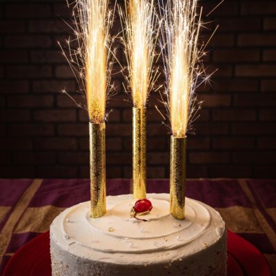 Three gold sparkler fountain candles shooting sparks on top of a white frosted cake for birthday celebration in Gurgaon