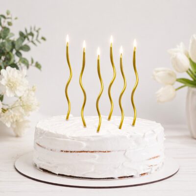Six gold spiral twisted birthday candles lit on a white frosted cake for birthday celebration in Gurgaon