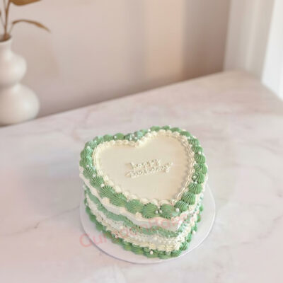 Heart-shaped layered cake with green and white frosting for a birthday celebration