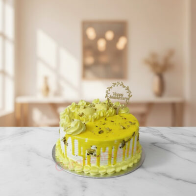 A vibrant yellow anniversary drip cake with pistachios and decorative frosting.