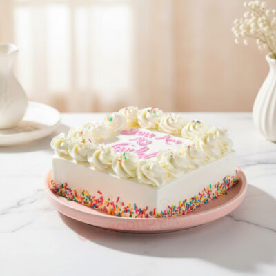 A beautifully designed square cake with creamy frosting and colorful sprinkles on a pastel pink plate.