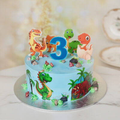 Dino themed birthday cake decorated with colorful dinosaur toppers and vibrant blue frosting in Gurgaon | Gurgaon Bakers