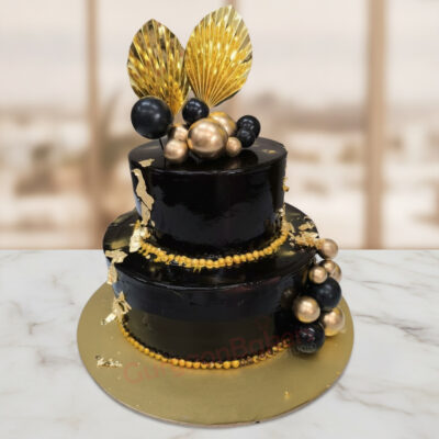 Elegant two-tier black and gold work anniversary cake with decorative elements in Gurgaon | Gurgaon Bakers